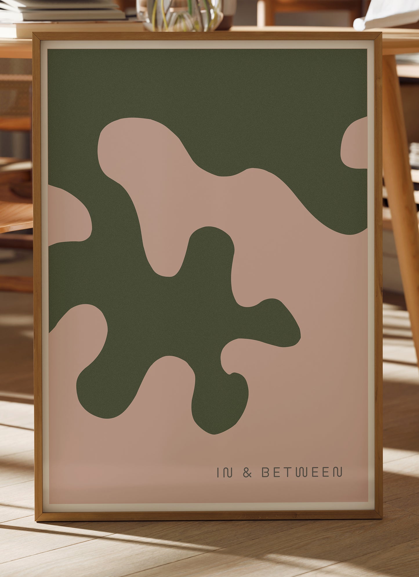 Lifestyle image with art print of large forest green oak leaf on soft peach background in natural wooden frame.
