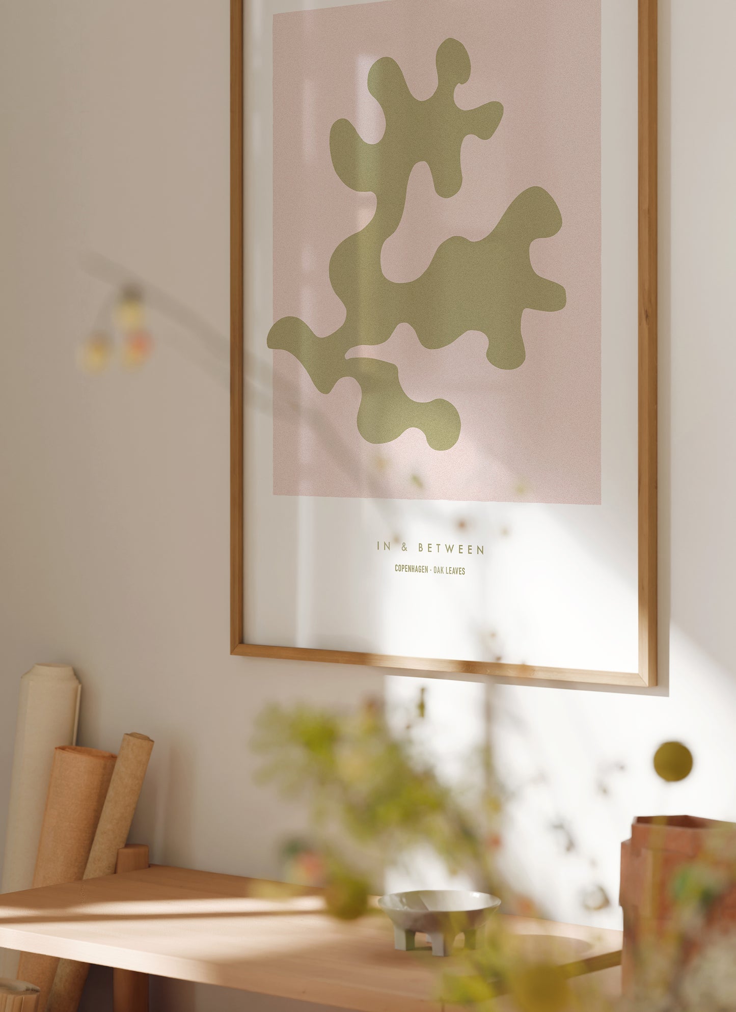 Lifestyle setting with In and Between art print of gold oak leaf on soft pink background in natural wooden frame.