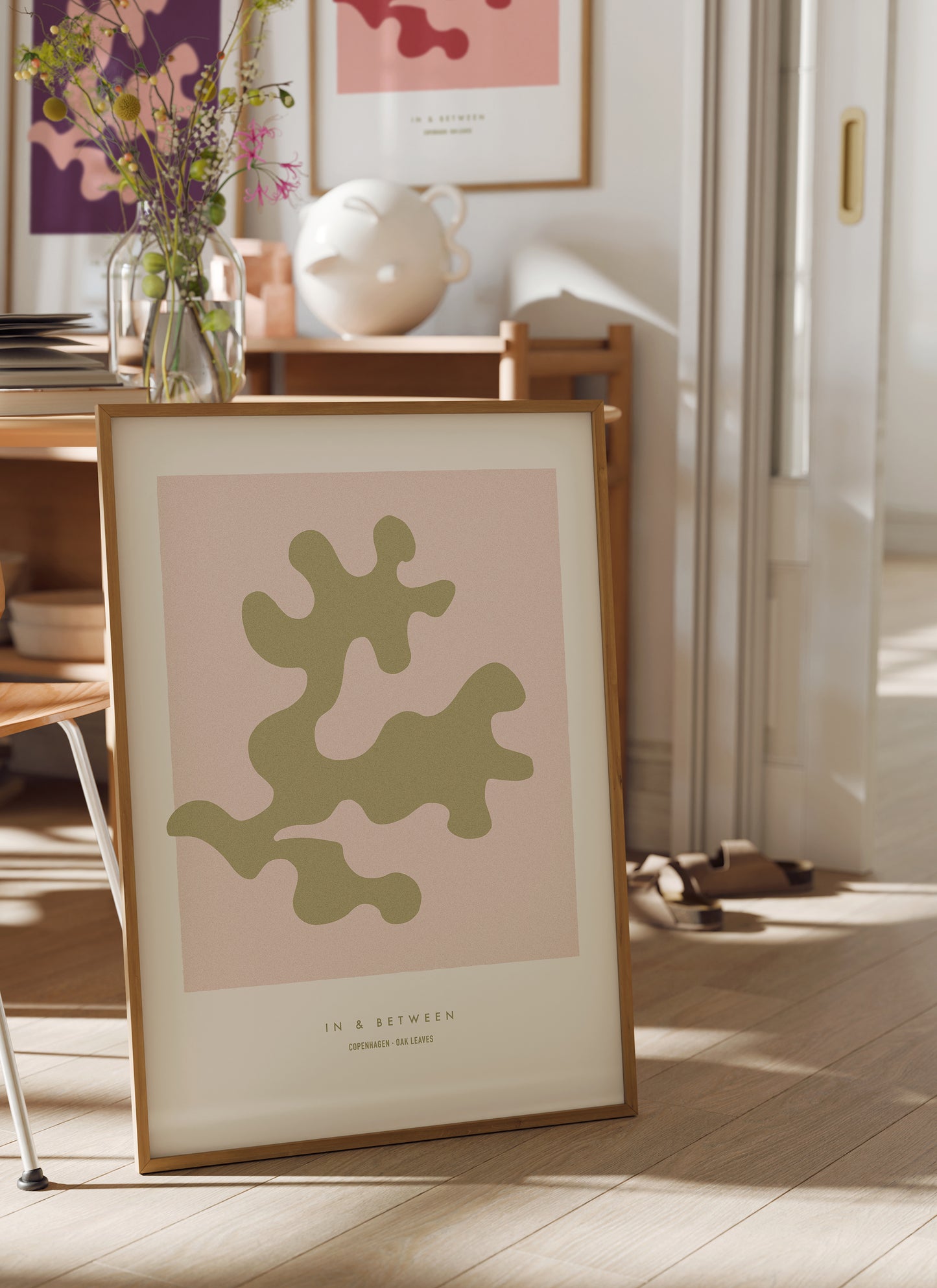 Lifestyle setting with In and Between art print of gold oak leaf on soft pink background in natural wooden frame.