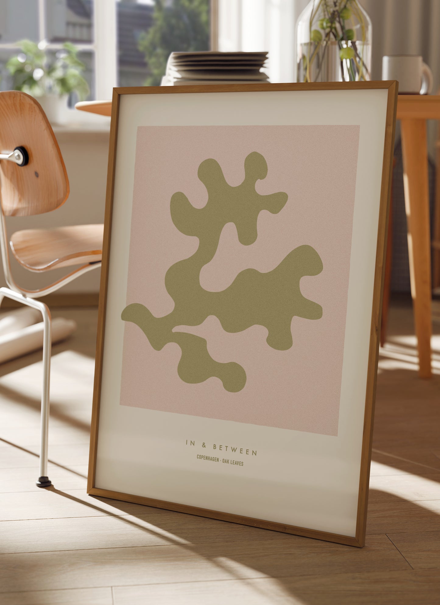 Lifestyle setting with In and Between art print of gold oak leaf on soft pink background in natural wooden frame.