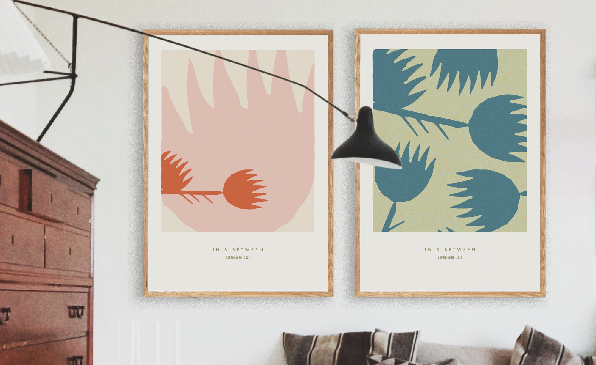 Art wall over a cushioned bench with two natural wood framed art prints of waterlilies in simple composition in cream/red and green/blue.