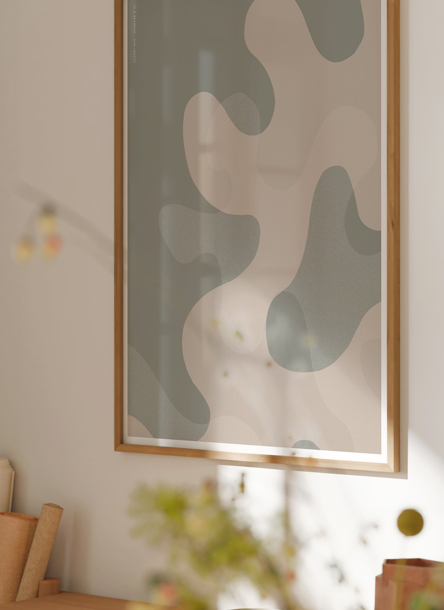 Lifestyle image with In and Between art print of large warm grey oak leaf shapes and background in natural wooden frame.