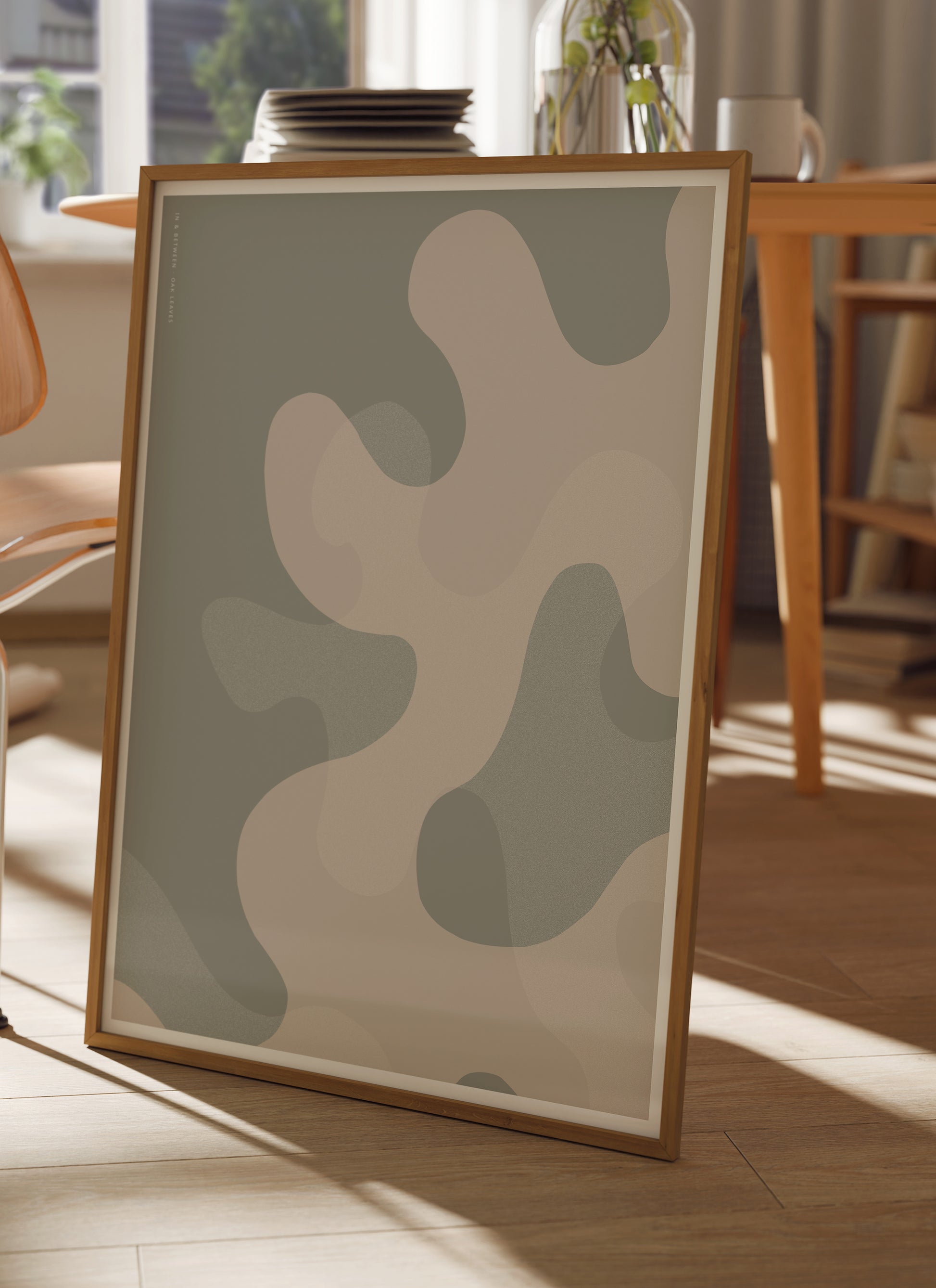 Lifestyle image with In and Between art print of large warm grey oak leaf shapes and background in natural wooden frame.